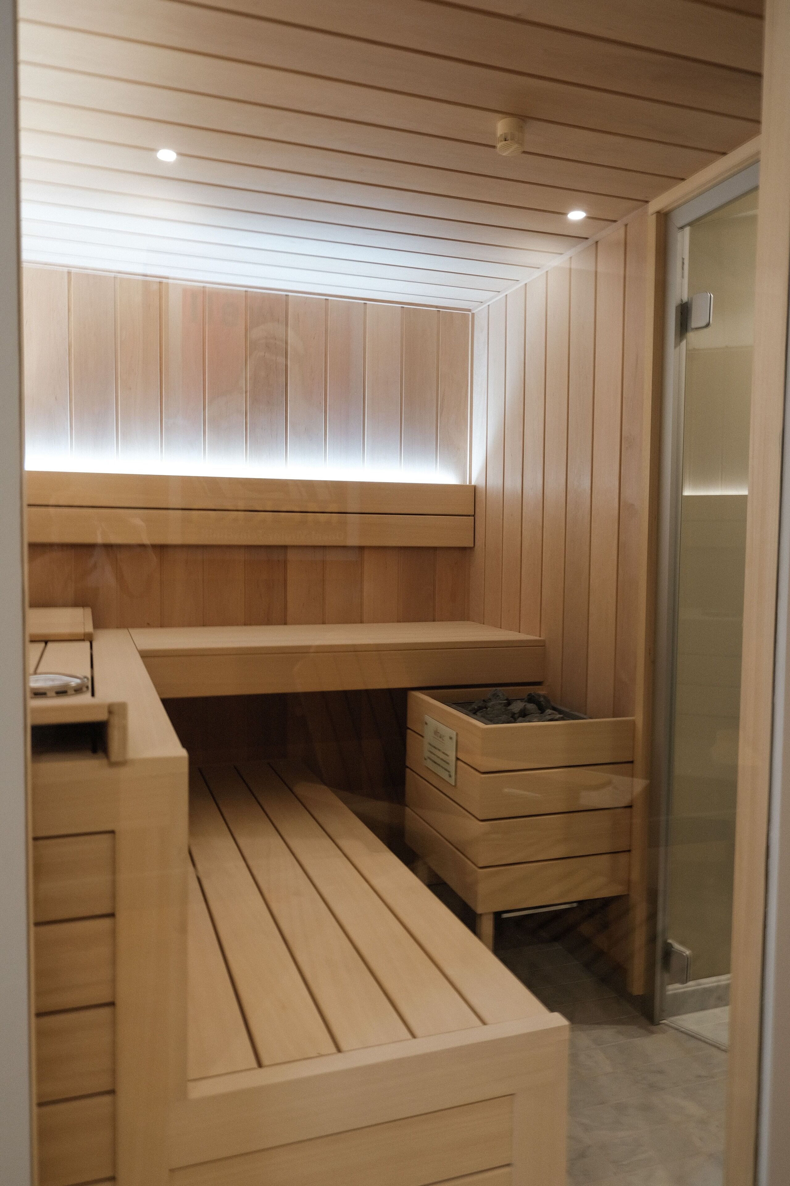 Un sauna aux murs et aux bancs en bois, avec une porte en verre et un petit banc sur lequel est posé un panneau.