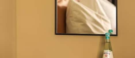 Fotografía enmarco de una cama con almohadas, una lámpara fijada a la pared y una botella de agua sobre una mesa.