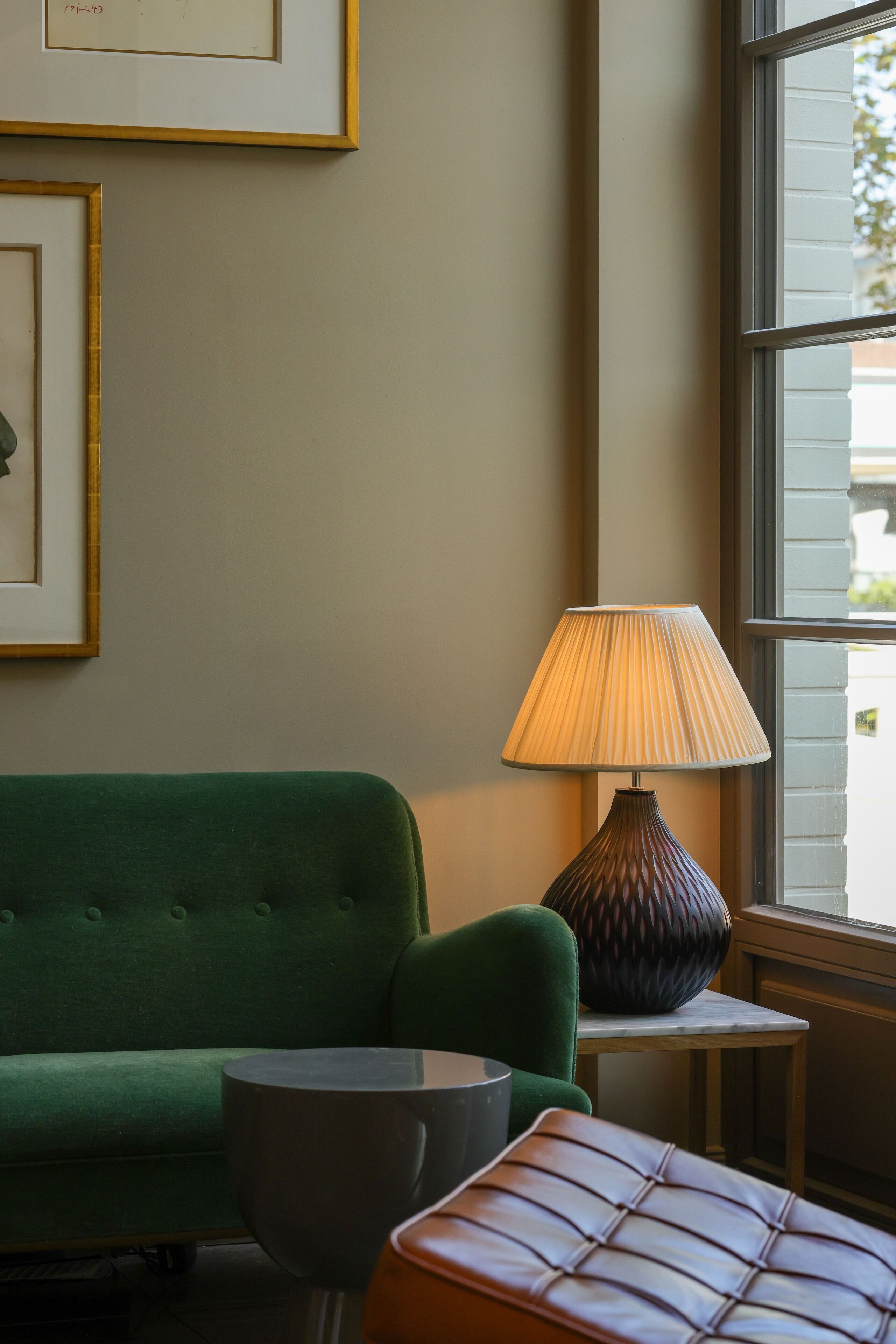 A green sofa, a lamp, and a small table in a room with a window.