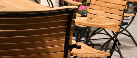 Outdoor wooden chairs and tables with metal frames, arranged in a patio area with a white brick wall and green metal gates.