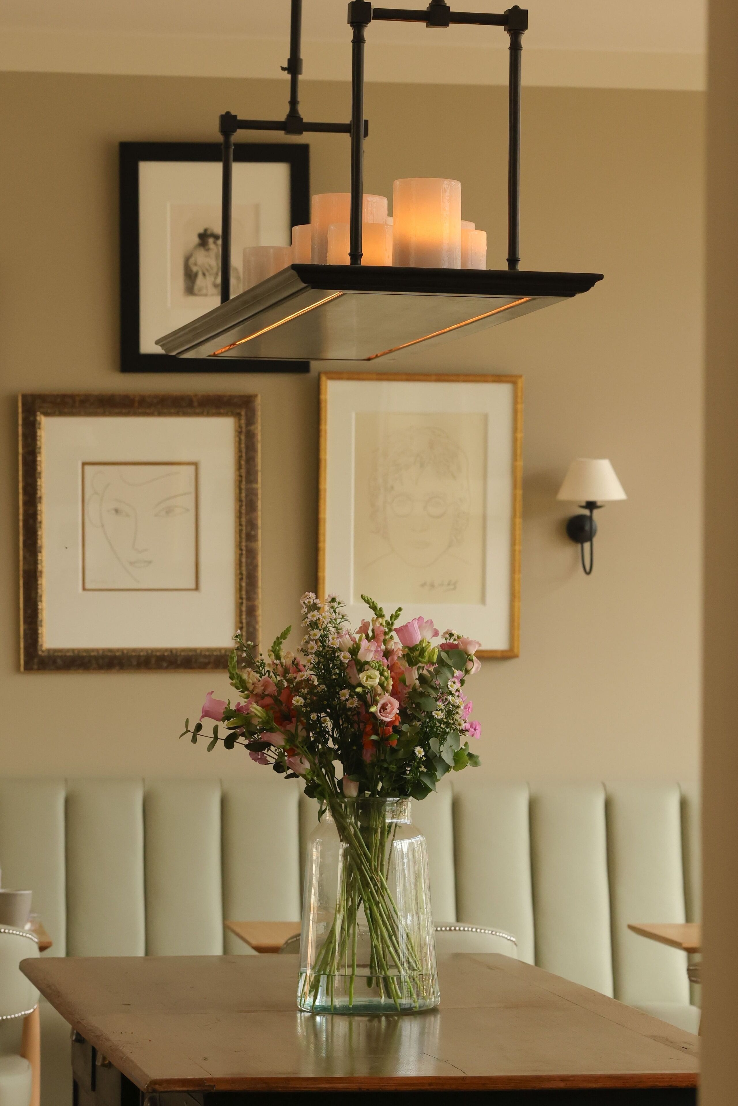 A dining area with a table, a vase of flowers, framed artwork, and a wall-mounted lamp.