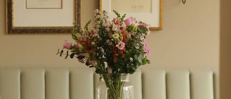 A dining area with a table, a vase of flowers, framed artwork, and a wall-mounted lamp.