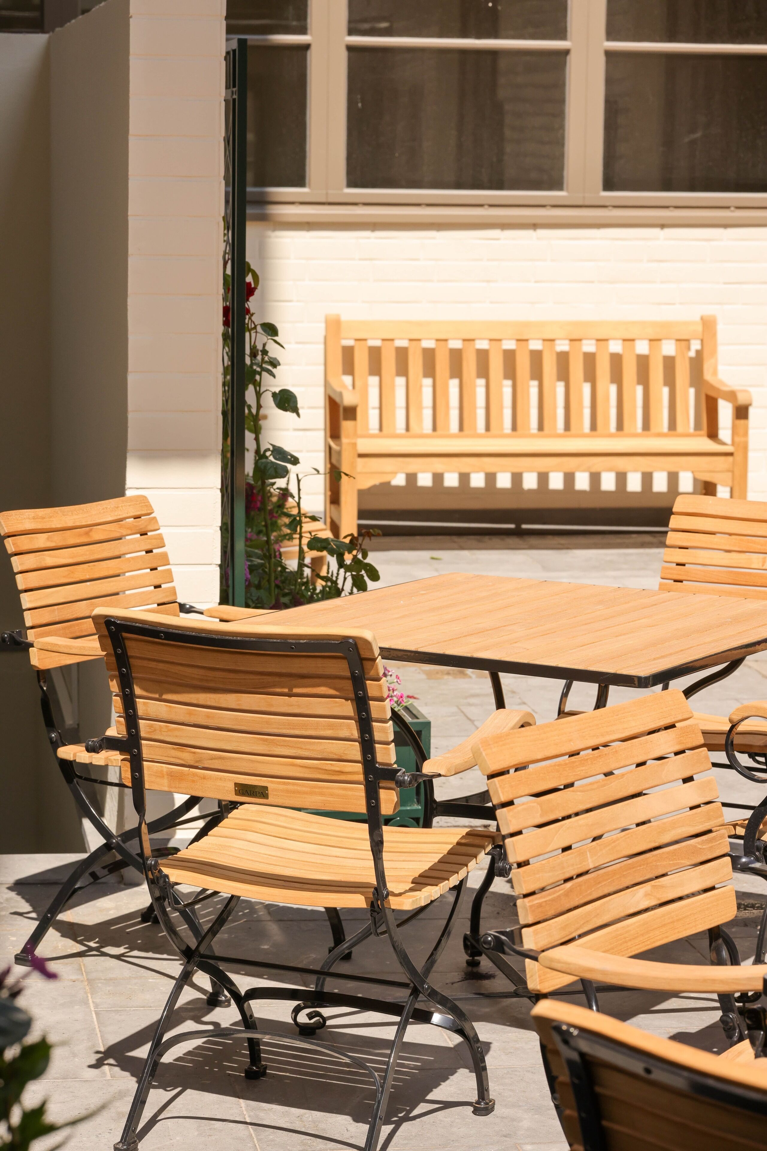 Un espace extérieur aménagé avec des meubles en bois, comprenant une table et des chaises, un banc et un pot de fleurs.