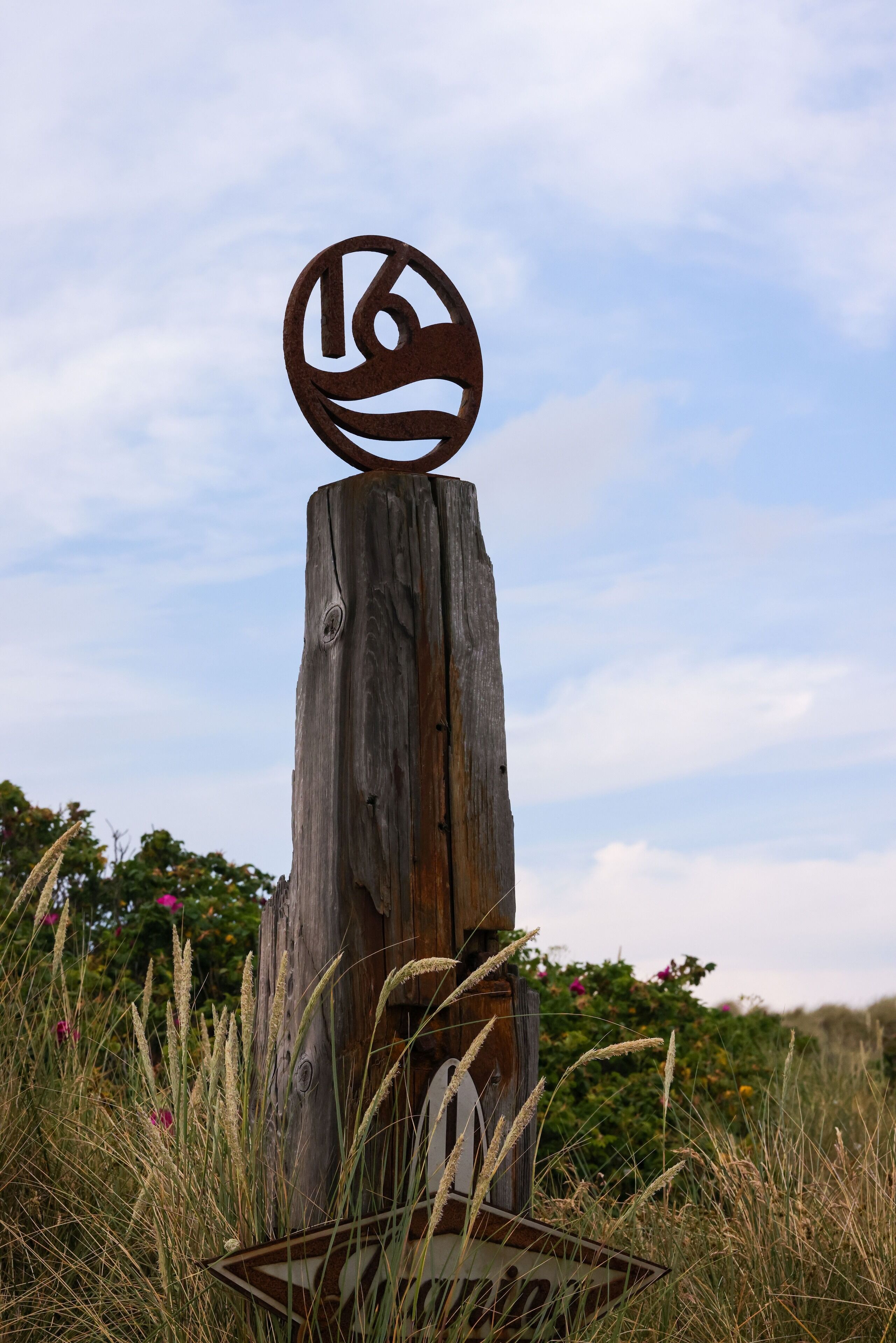 A rustic wooden post with a circular metal emblem featuring a stylized face.