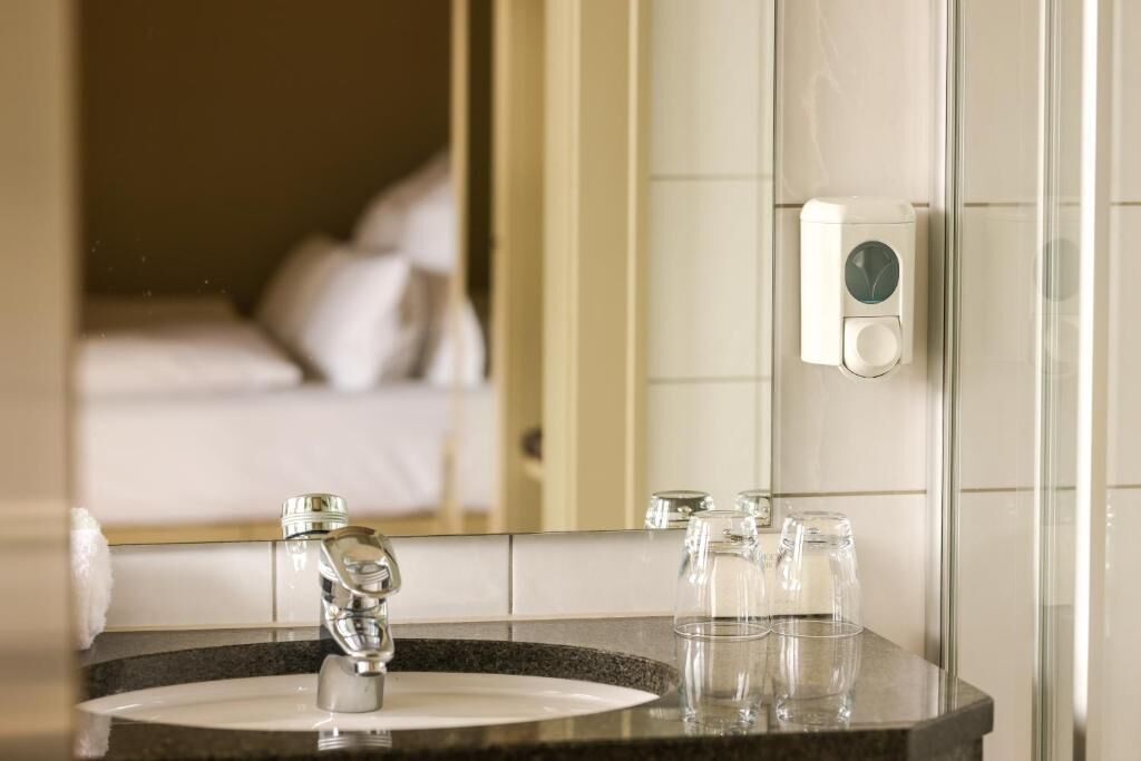 Un baño con lavamanos, espejo y dispensador de jabón.