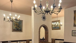 L’intérieur d’un restaurant, avec de nombreuses tables et chaises, un lustre et des œuvres d’art encadrées accrochées aux murs.