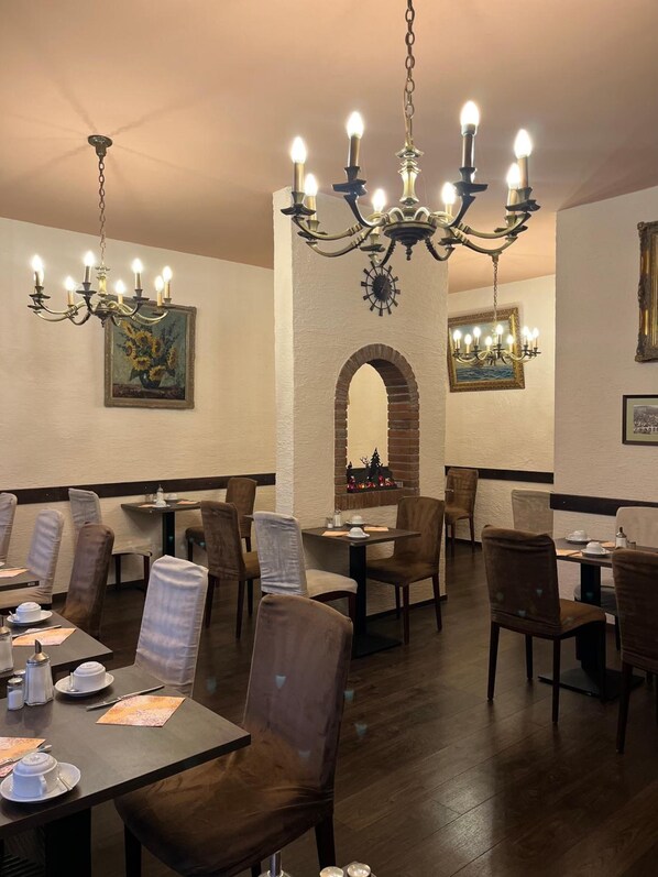 A restaurant interior with multiple tables and chairs, a chandelier, and framed artwork on the walls.