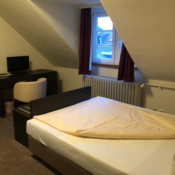 Ein Schlafzimmer mit einem Bett, einem Schreibtisch, einem Stuhl und einem Fenster mit Vorhängen.