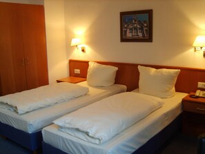 Ein Hotelzimmer mit zwei Einzelbetten, einem Holzschrank, Nachttischlampen und einem gerahmten Bild an der Wand.