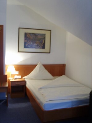 Ein Hotelzimmer mit einem Einzelbett, einem Nachttisch mit Lampe und einem gerahmten Bild an der Wand.