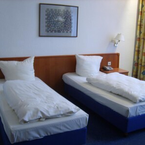 Ein Hotelzimmer mit zwei Einzelbetten, einem Holzkopfteil, einem Nachttisch mit Lampe und einem gerahmten Bild an der Wand.