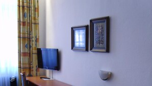 A hotel room with a desk, two chairs, a television, and two framed pictures on the wall. - Hotel Vier Jahreszeiten (Heidelberg)