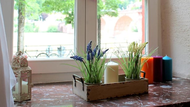 Une fenêtre ornée d’un motif en forme de cœur, une bougie et une plante dans un pot en bois.