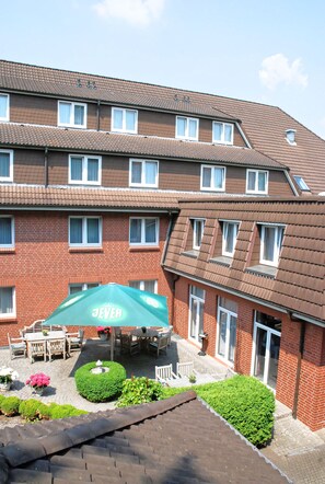 Ein mehrstöckiges Hotel mit Backsteinfassade, zahlreichen Fenstern und einem Innenhof mit Außenbestuhlung und Grünpflanzen.