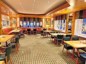 A hotel dining area with multiple seating options including booths and tables, a checkered floor pattern, and large windows with decorative star-shaped elements.