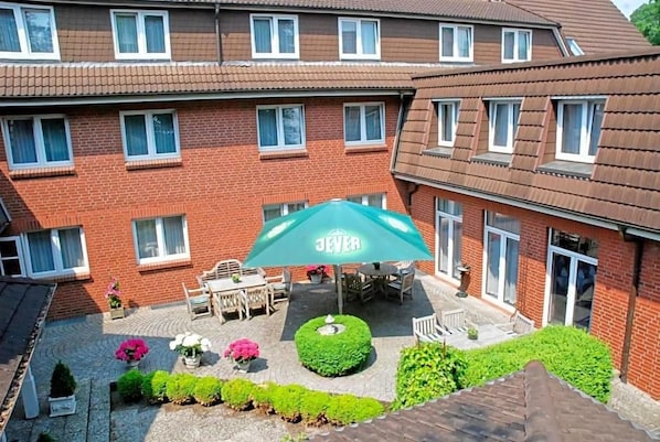 A multi-story brick building with a patio area featuring outdoor furniture and a green umbrella.