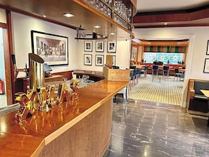 A hotel lobby with a reception desk, framed artwork on the walls, and a seating area with tables and chairs.