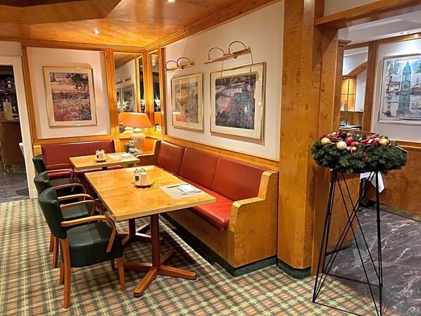 A restaurant with a wooden table and red cushioned bench seating, framed pictures on the wall, and a Christmas tree.