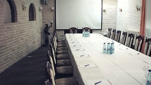 A conference room with a long table, chairs, a projector screen, and a brick wall. - Hotel & Restaurant Bei Baki (Sehnde)