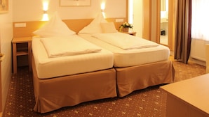 A hotel room with two beds, a bedside table with a lamp, a mirror, and a view of the bathroom. - Hotel & Restaurant Bei Baki (Sehnde)