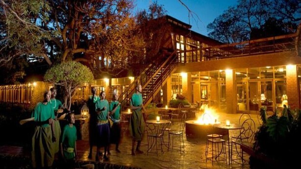 A building with a staircase leading to a second floor, surrounded by trees and outdoor seating areas with tables and chairs.