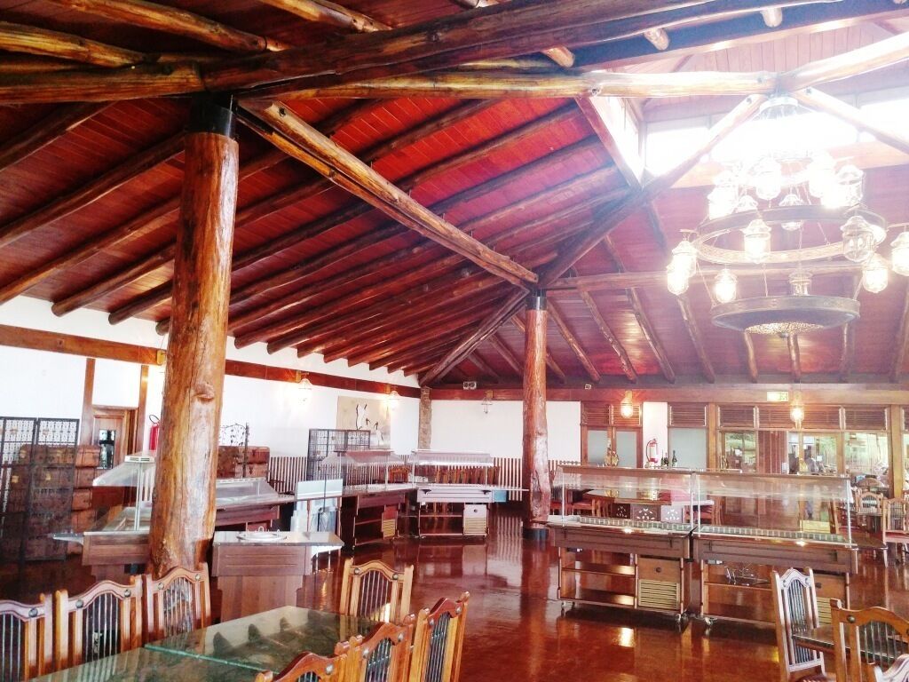 Un restaurant spacieux avec des poutres en bois et un plafond haut. Les tables et les chaises sont disposées pour accueillir les clients.