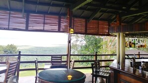 A covered outdoor seating area with a table and chairs, a bar with bottles, and a view of the landscape.