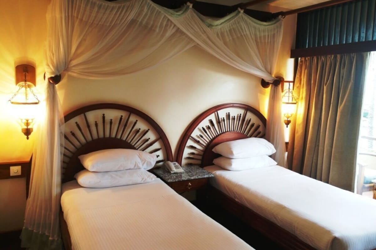 A hotel room with two beds, a canopy, bedside lamps, and a telephone on the nightstand.
