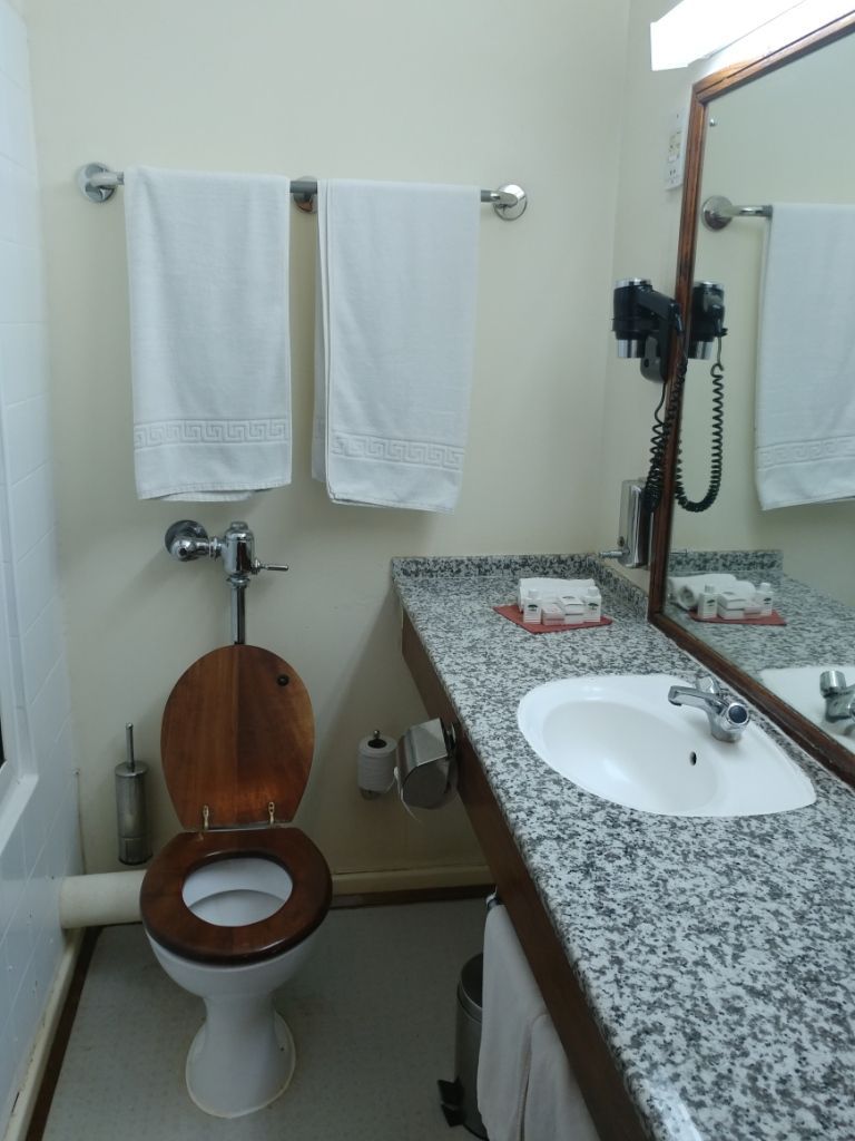 A bathroom with a wooden toilet, a white sink, a mirror, and towels on a rack.