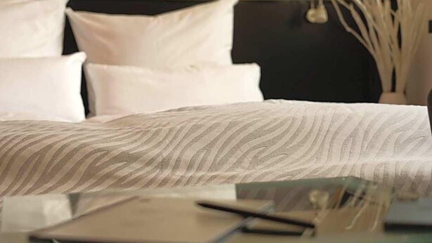 A bed with a patterned bedspread, a bedside table with a laptop, and white pillows.