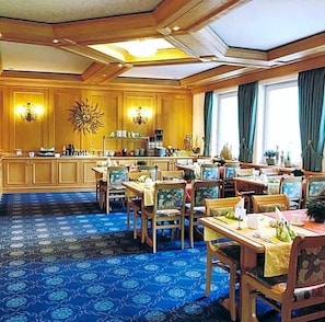 A hotel dining area with wooden furniture, a patterned carpet, and a sunburst wall decoration.