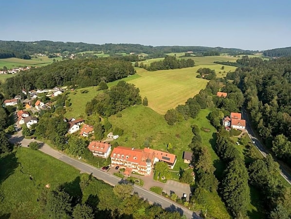 An aerial view of a rural area with a large estate featuring multiple buildings, a well-maintained lawn, and surrounding greenery.
