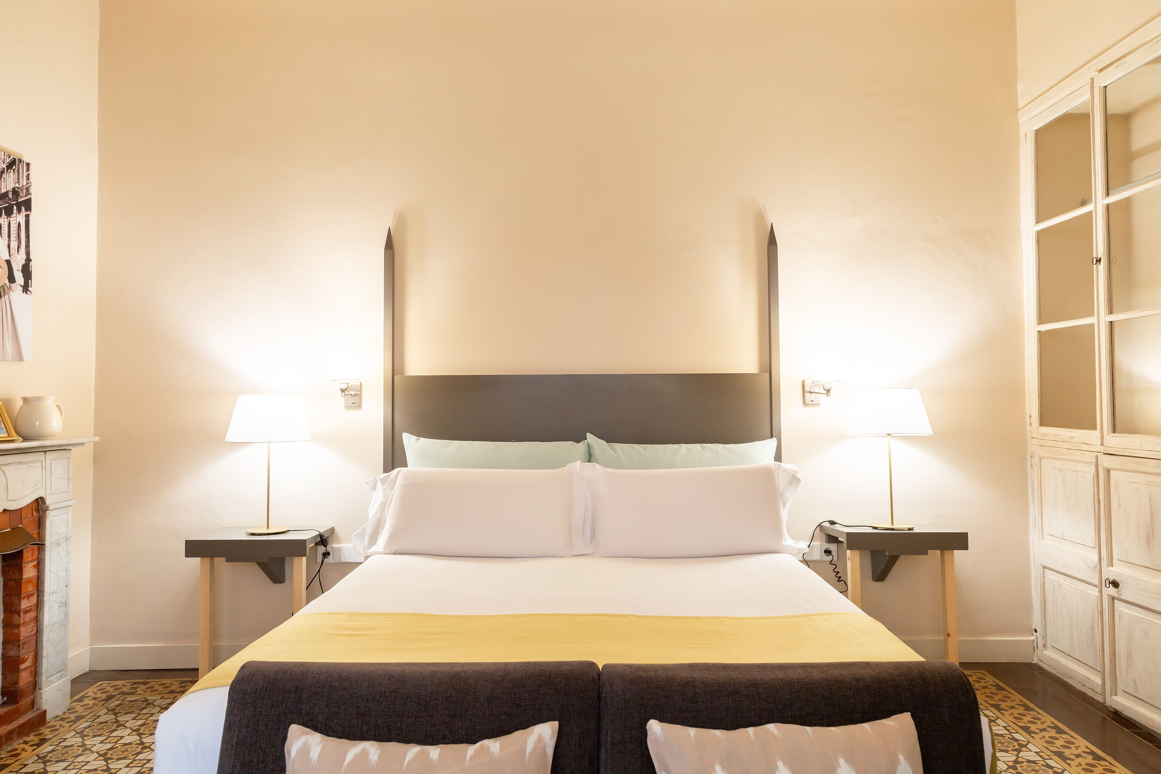 A hotel room with a large bed, two bedside tables with lamps, a chest of drawers, and a patterned floor.