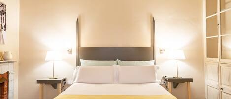 A hotel room with a large bed, two bedside tables with lamps, a chest of drawers, and a patterned floor.