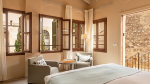 A hotel room with a bed, two armchairs, a small table with a tray, and large windows with shutters.