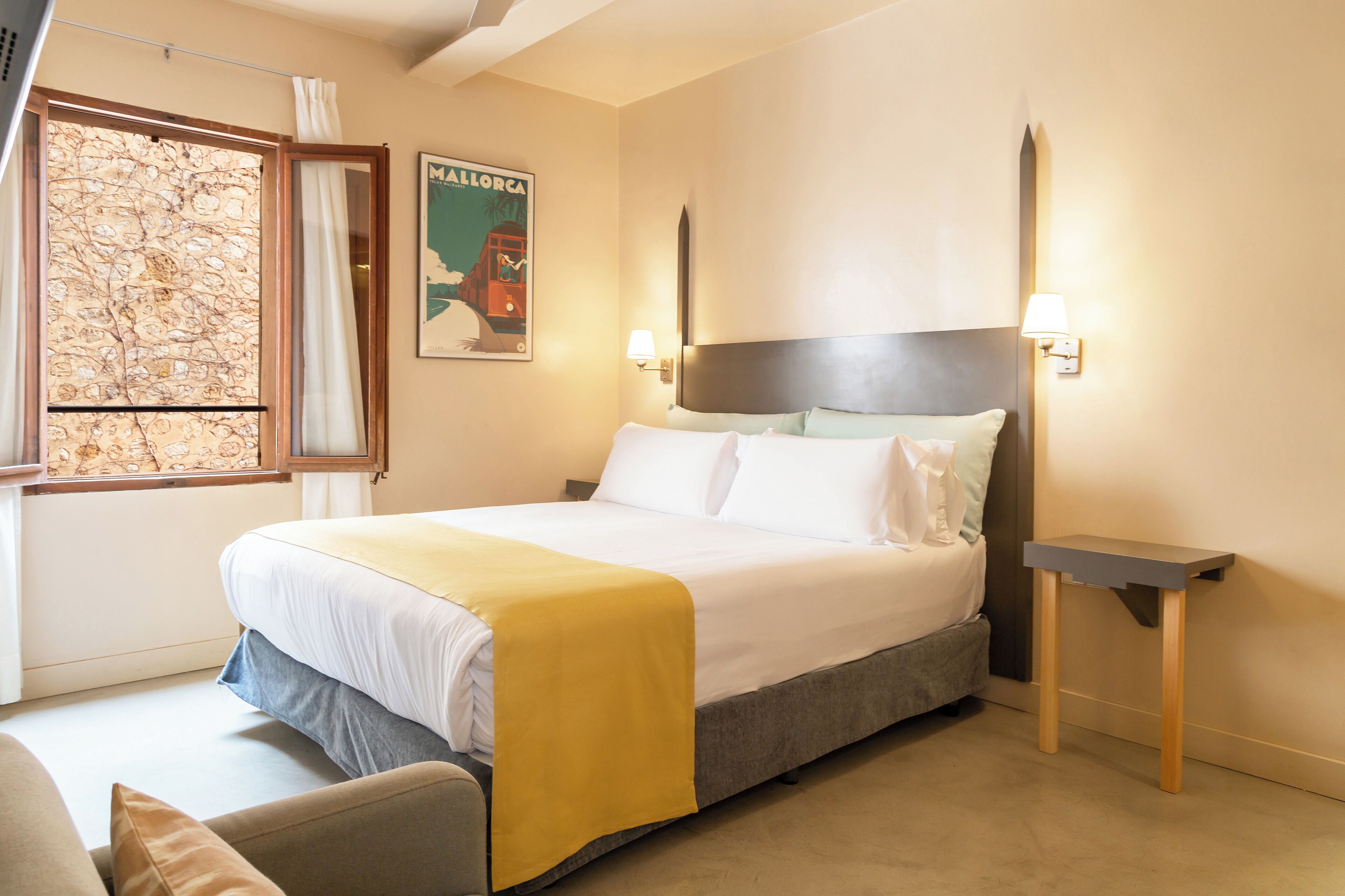 Habitación de hotel con cama, mesita de noche, un mapa en la pared y una ventana con cortinas.