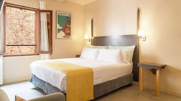 Habitación de hotel con cama, mesita de noche, un mapa en la pared y una ventana con cortinas.