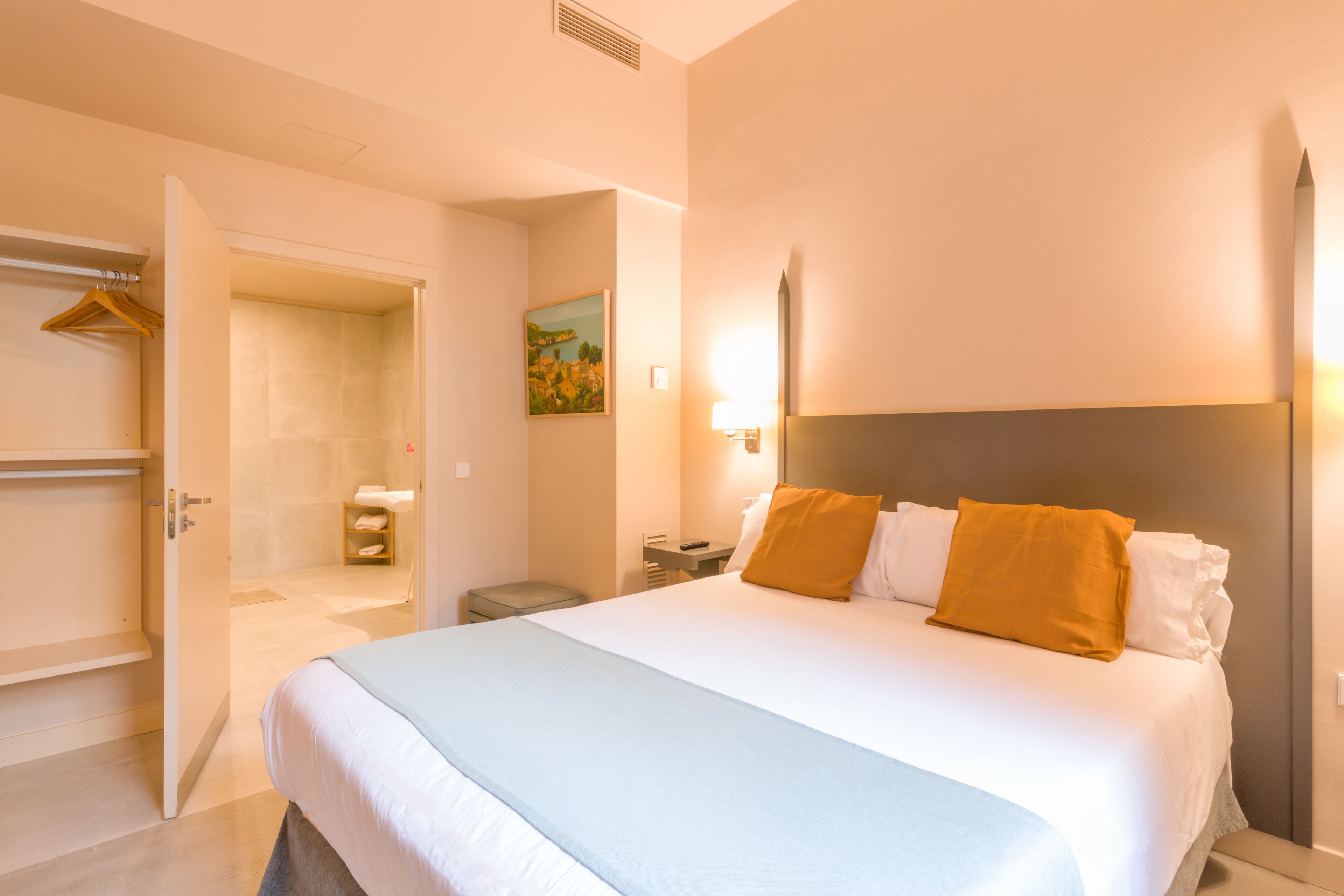 A hotel room with a large bed, a bedside table, a nightstand, a wardrobe, and a bathroom visible through an open door.