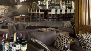 A spacious lounge area with leather sofas, a bar with multiple chairs, and a stone wall. - Seronera Wildlife Lodge (Serengeti)