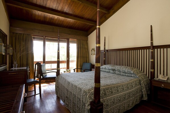 A bedroom with a four-poster bed, wooden furniture, and a view of the outdoors.