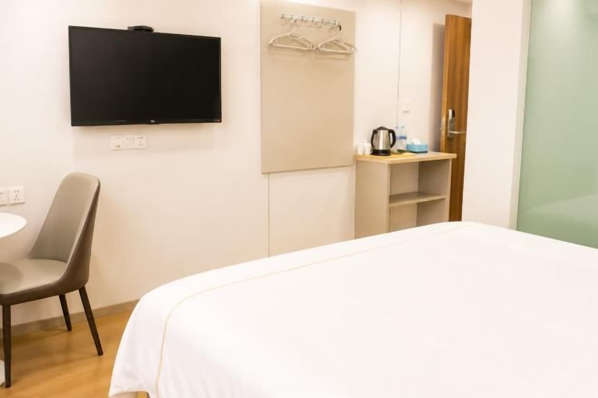 Habitación de hotel con cama, escritorio, silla, televisor, perchero y espejo.
