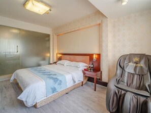 Habitación de hotel con cama, mesita de noche, lámpara y sillón de masajes.