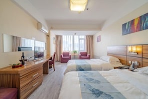 Une chambre d’hôtel avec deux lits, un bureau avec une télévision, une chaise et une petite table avec une plante.