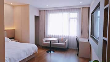 A hotel room with a bed, a small round table, a sofa, a TV, and a window with curtains.
