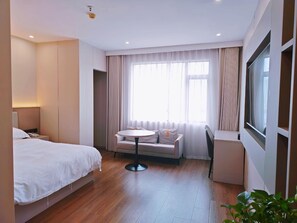 A hotel room with a bed, a small round table, a sofa, a TV, and a window with curtains.