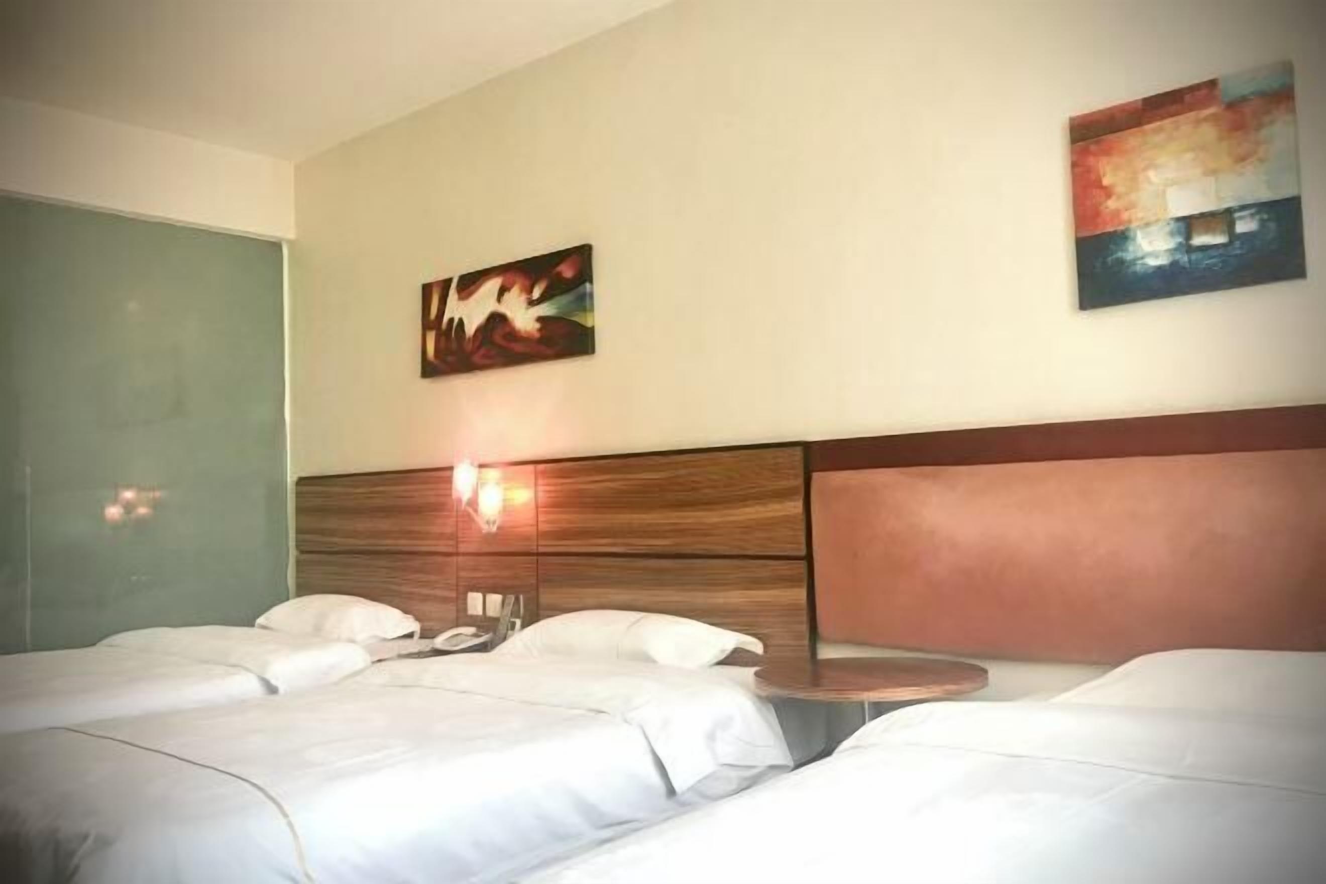A hotel room with two beds, a wooden headboard, a bedside table, and two wall-mounted paintings.