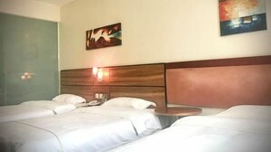 Quarto de hotel com duas camas, cabeceira de madeira, mesa de cabeceira e dois quadros pendurados na parede.