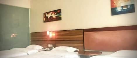 A hotel room with two beds, a wooden headboard, a bedside table, and two wall-mounted paintings.