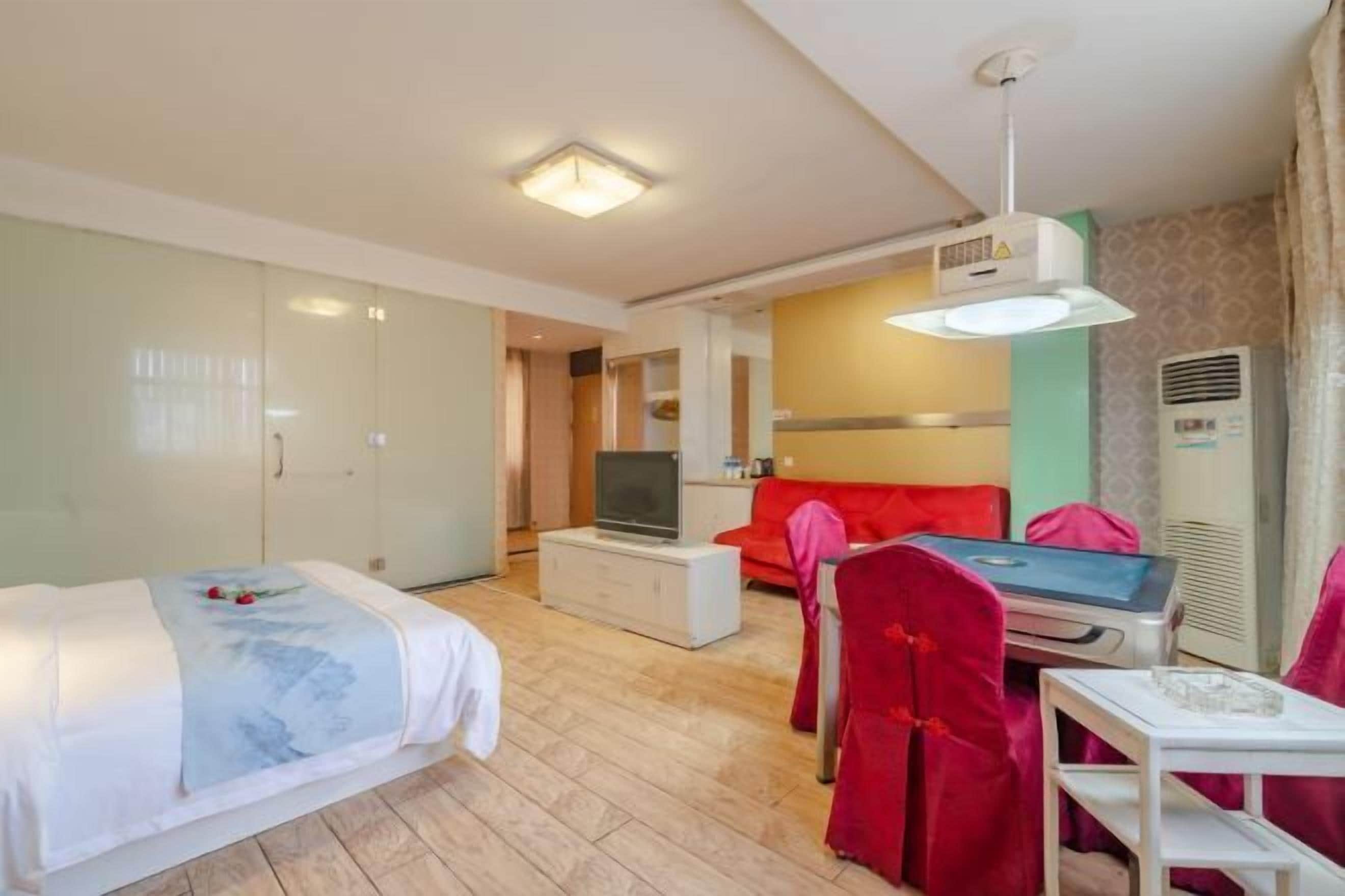 A hotel room with a bed, a TV on a white cabinet, a red sofa, and a small table with a chair.