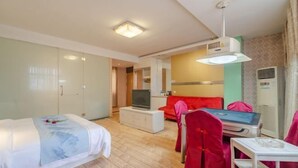 Quarto de hotel com cama, televisão sobre um armário branco, sofá vermelho e pequena mesa com uma cadeira.